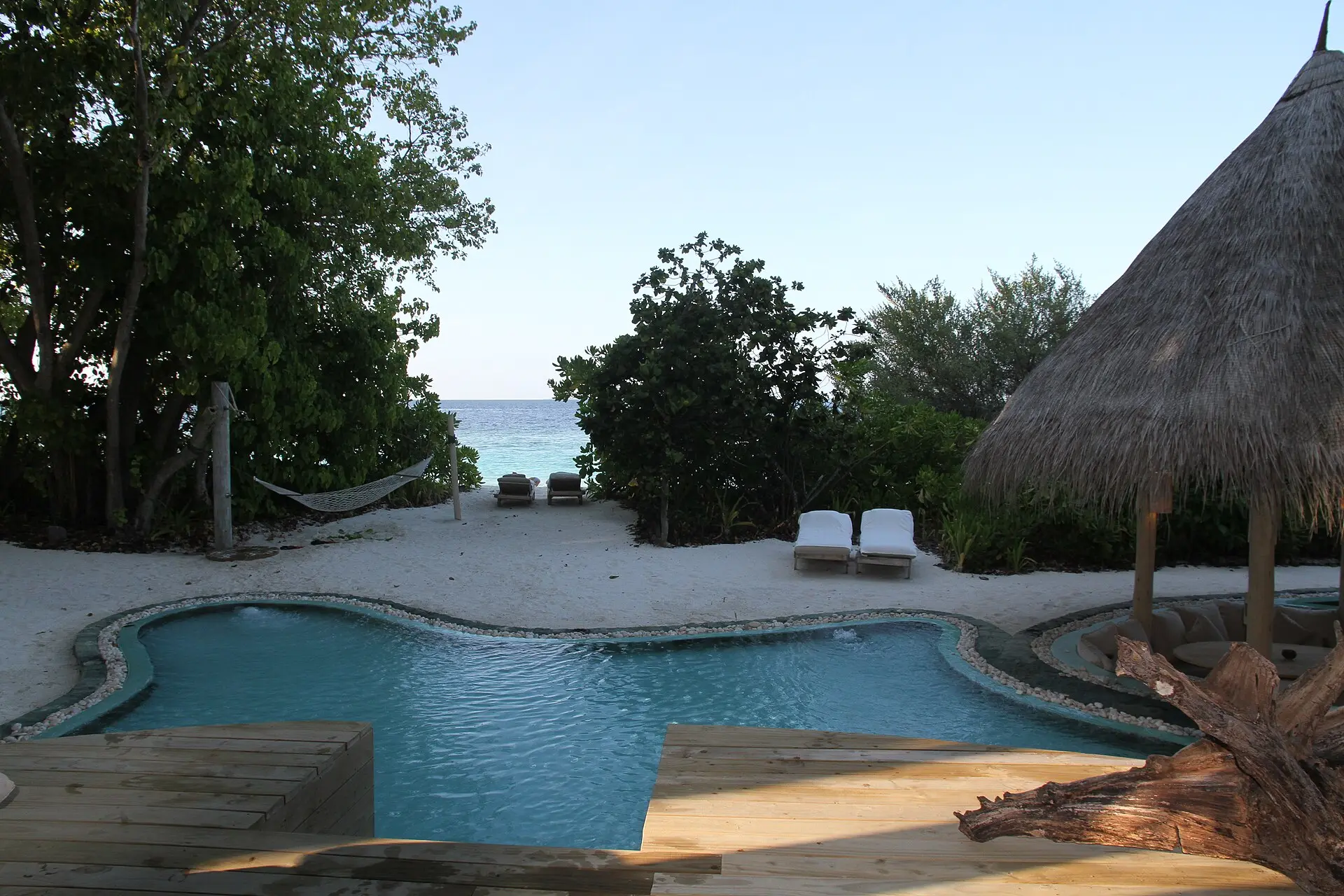A private pool with a thatched sala and loungers among trees at a villa on Soneva Fushi