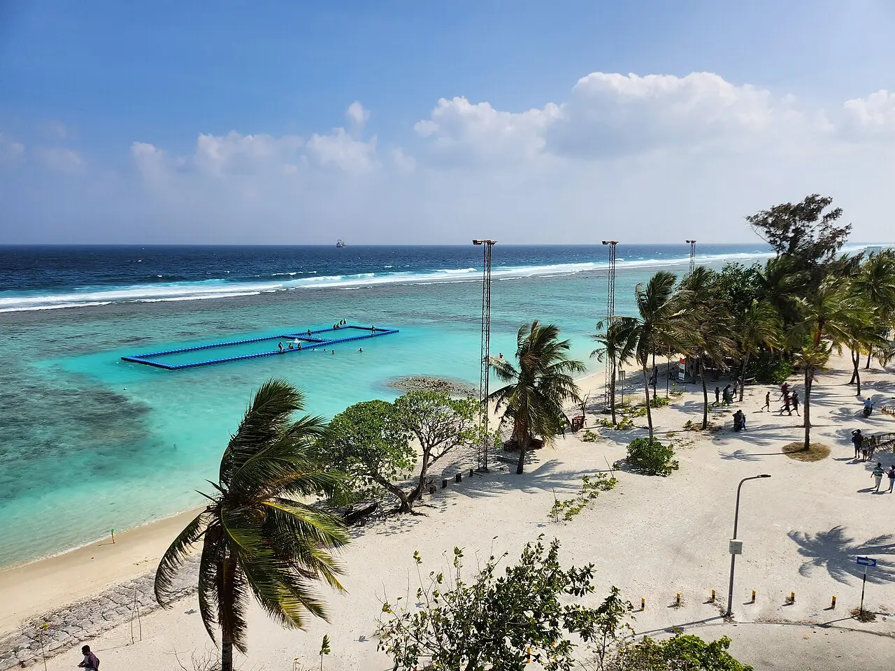 Elevated view of Hulhumalé beach with palm trees, white sand and a swimming enclosure in the lagoon