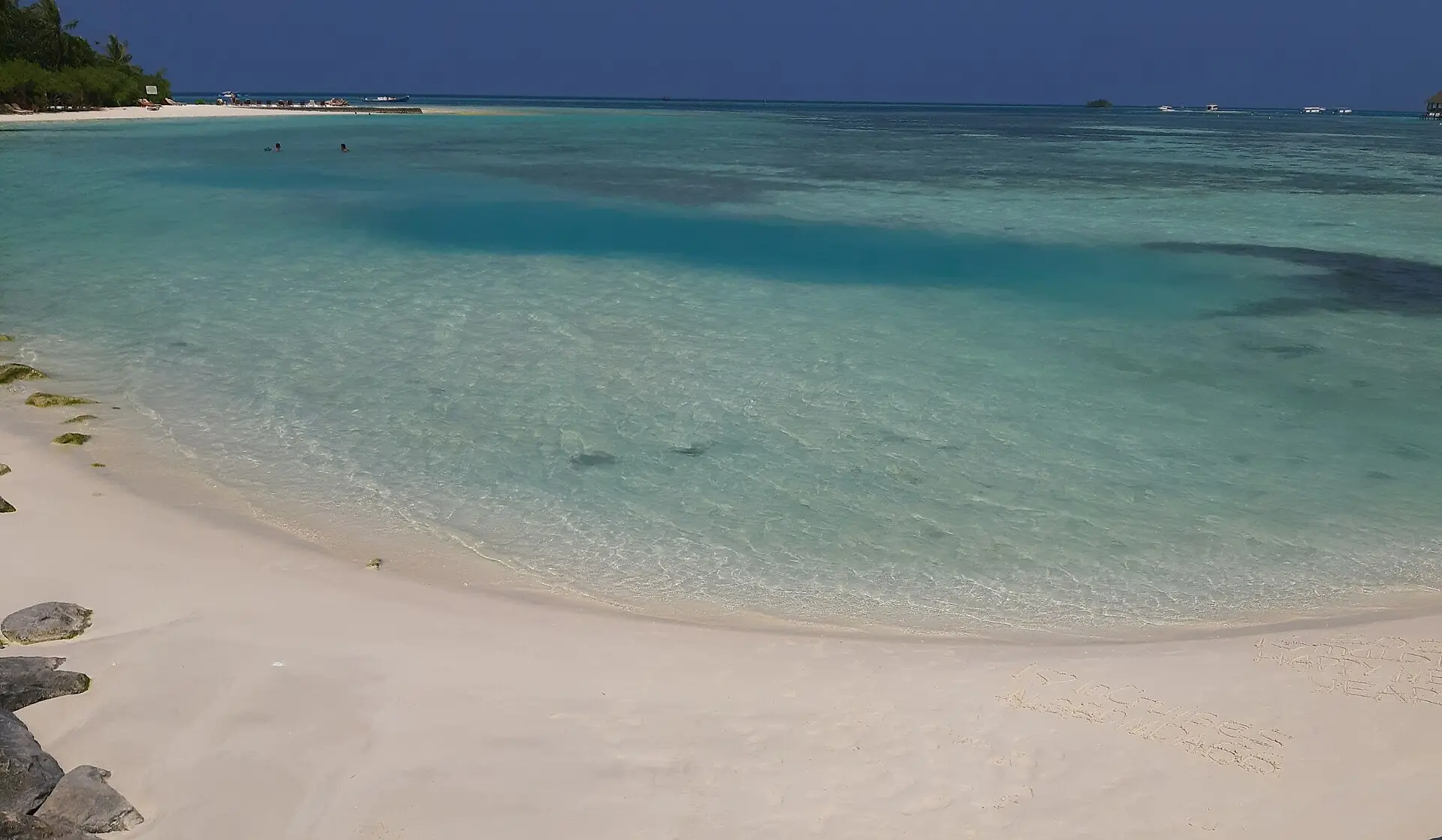A curve of soft white sand and clear turquoise shallows on a beach at Huraa