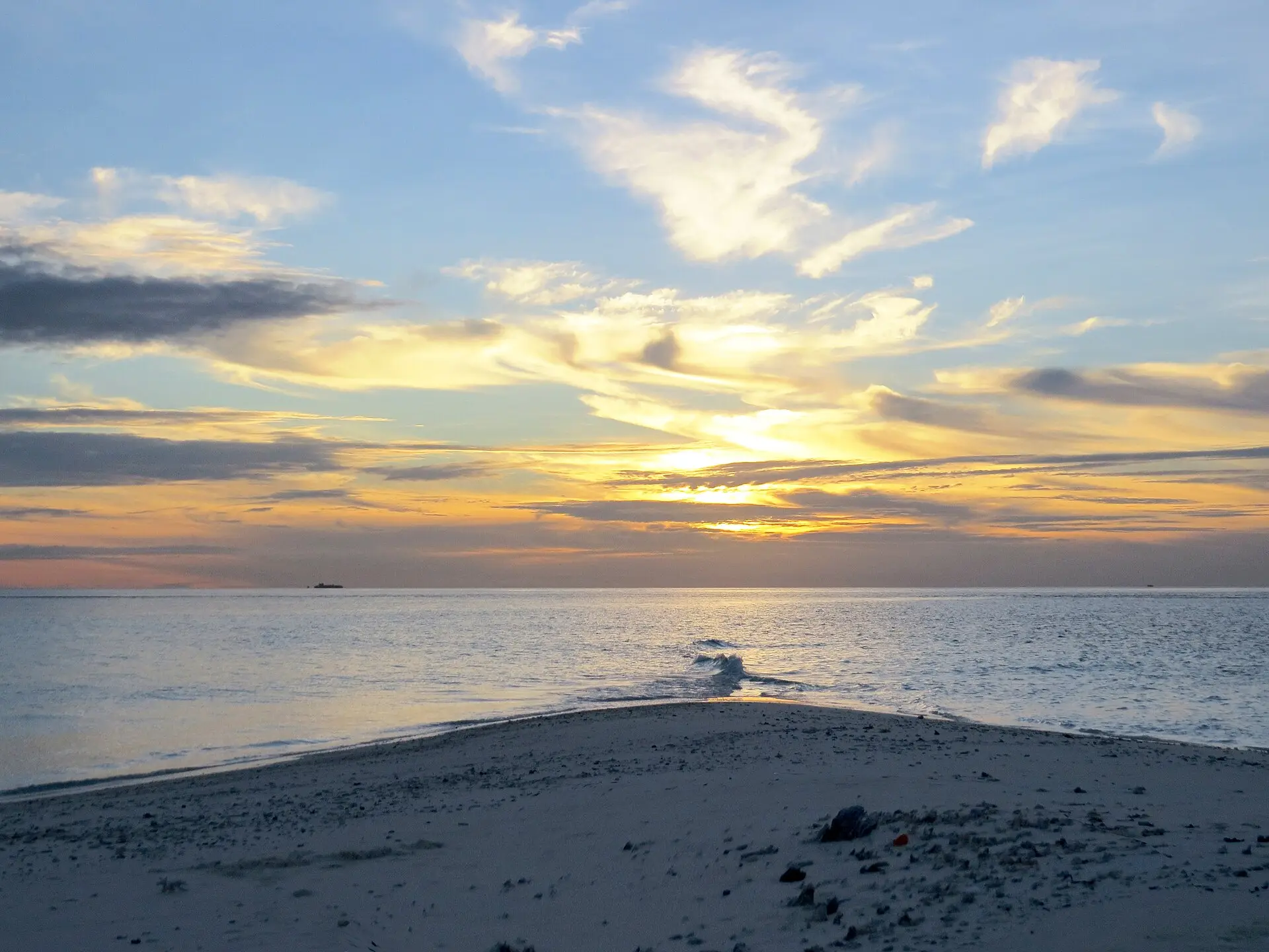 A narrow sandbank spit reaching into calm water at sunset in South Malé Atoll