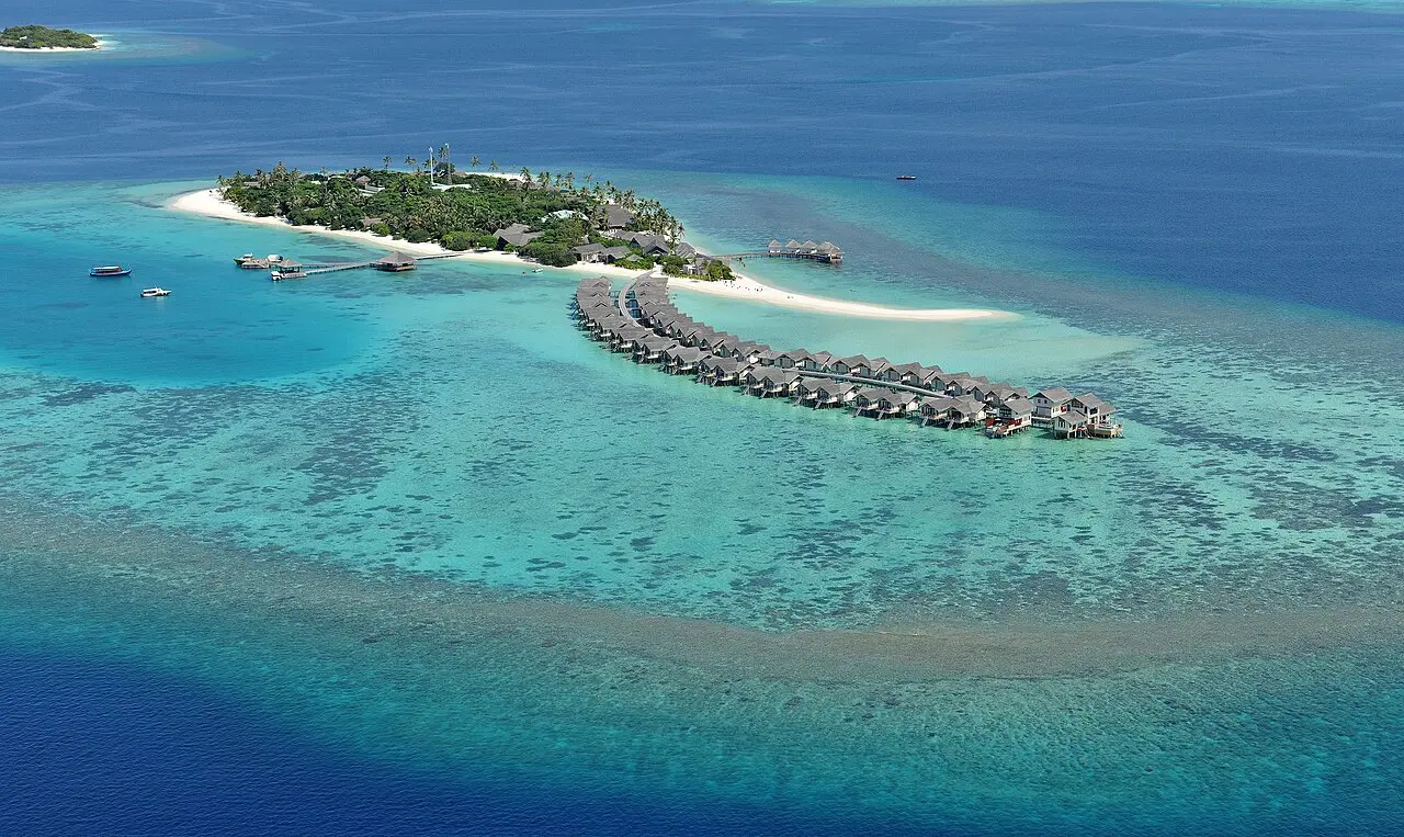 Aerial view of a resort on Maamigili in Raa Atoll with curving rows of water villas over the reef