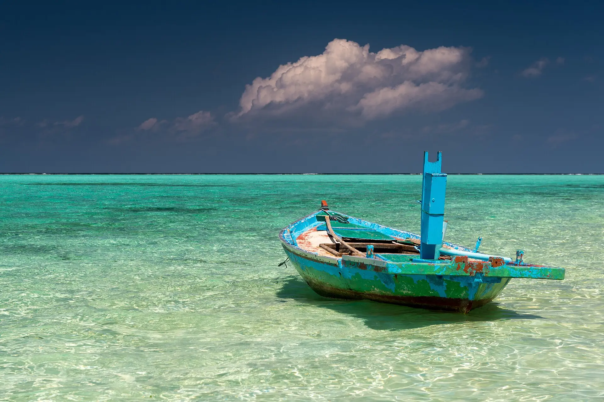 A weathered turquoise wooden boat sitting in clear shallow water off Thoddoo